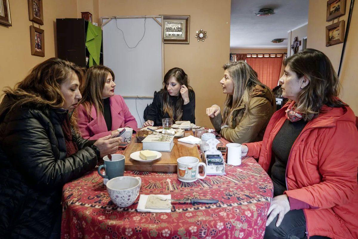 Cinque attiviste del collettivo Mosacat discutono attorno a un tavolo con tazze e cibo, in una casa.