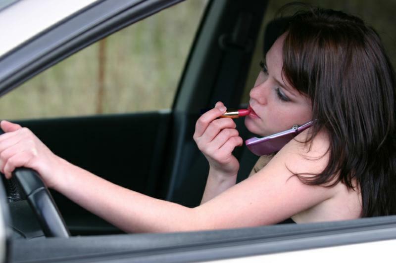 Multitasking alla guida di un'auto (ragazza mentre guida parla al cellulare e si dà il rossetto)